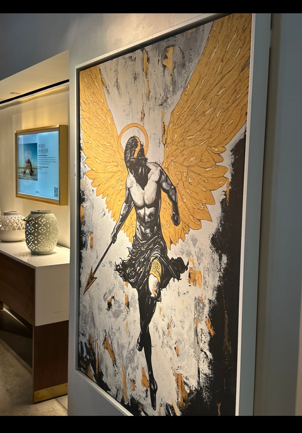 Framed artwork of an angel with gold wings in a room setting.
